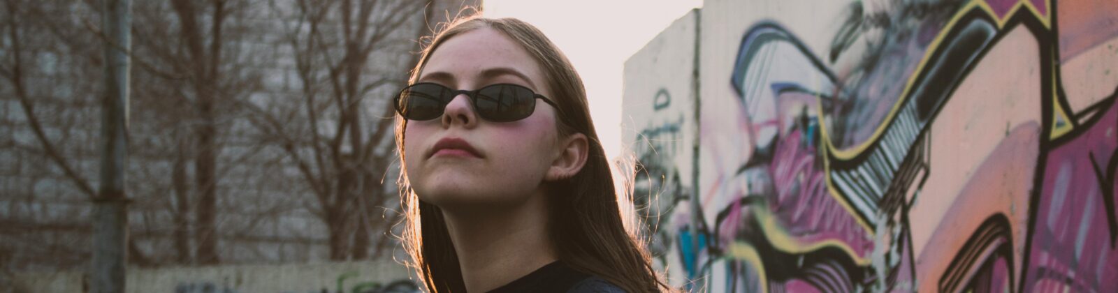 Young woman with sunglasses standing in front of a mural